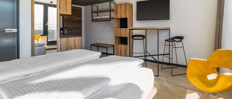 Una habitación de hotel moderna con una cama grande, un escritorio, un televisor y una silla amarilla.
