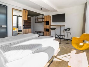 Une chambre d’hôtel moderne avec un grand lit, un bureau, une télévision et une chaise jaune.