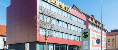 A B&B hotel with a modern facade, large windows, and a visible parking area.