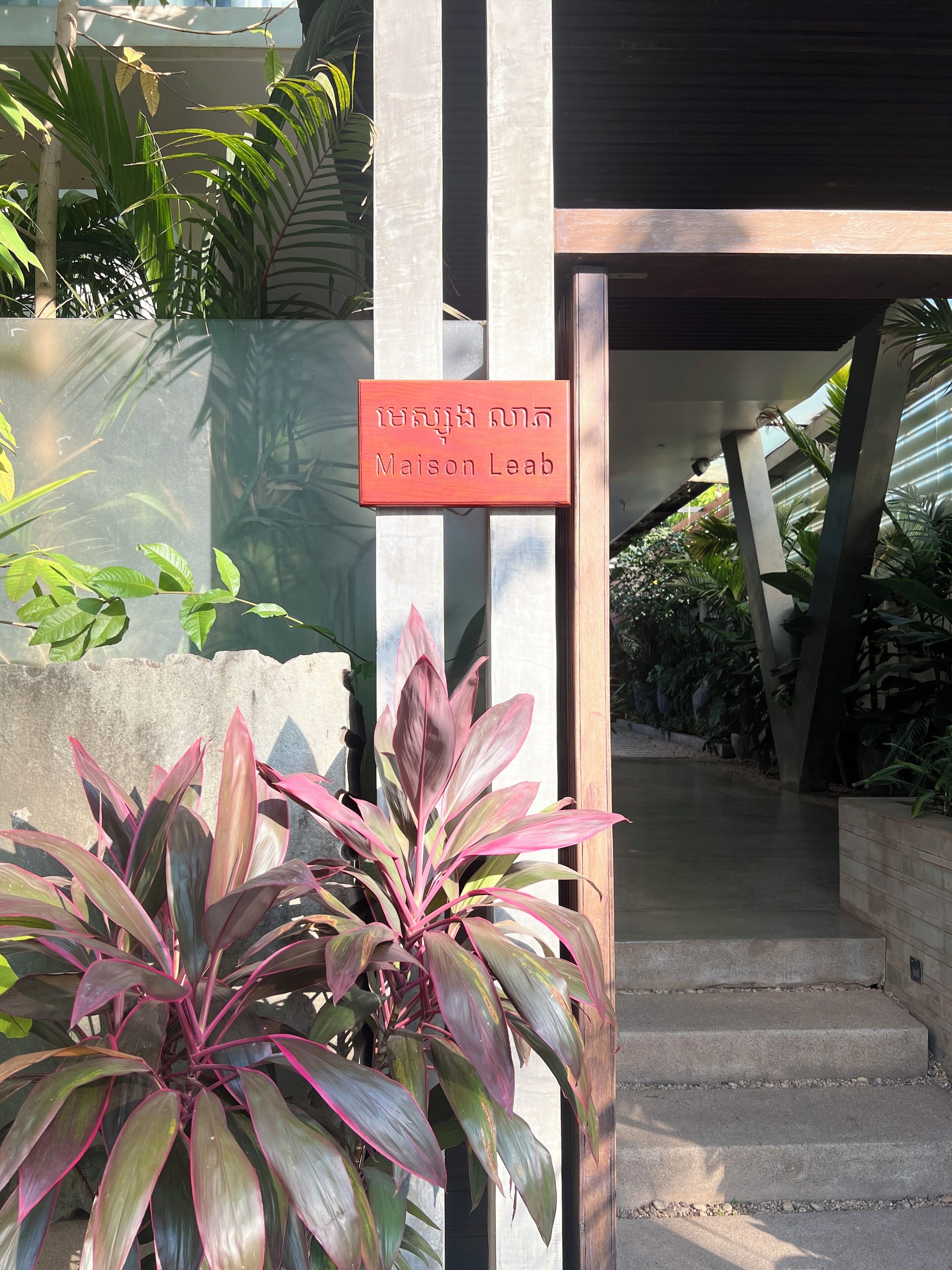 A sign reading "Maison Leab" in front of a building with a modern architectural design, featuring a concrete structure and a glass entrance.