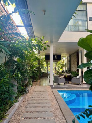 A covered outdoor area with a pool, surrounded by lush greenery and modern furniture. - Maison Leab (Siem Reap)