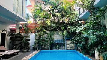 A swimming pool with tiled blue floor, surrounded by potted plants and lounge chairs.
