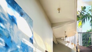 A hallway with a large abstract painting, a staircase, and a view of greenery outside. - Maison Leab (Siem Reap)