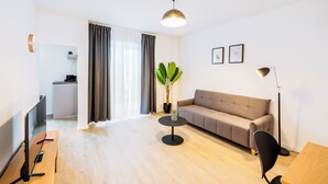 A modern living room with a sofa, a coffee table, a TV, and a desk. - Glück Auf Appartements Herkulesstraße (Essen)