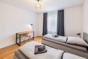 A modern bedroom with two single beds, a desk, and a chair.