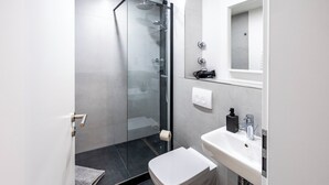 A modern bathroom with a glass-enclosed shower, a white toilet, and a sink with a mirror above it. - Glück Auf Appartements Herkulesstraße (Essen)