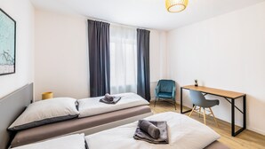 A room with two beds, a desk, a chair, and a hanging light fixture. - Glück Auf Appartements Herkulesstraße (Essen)