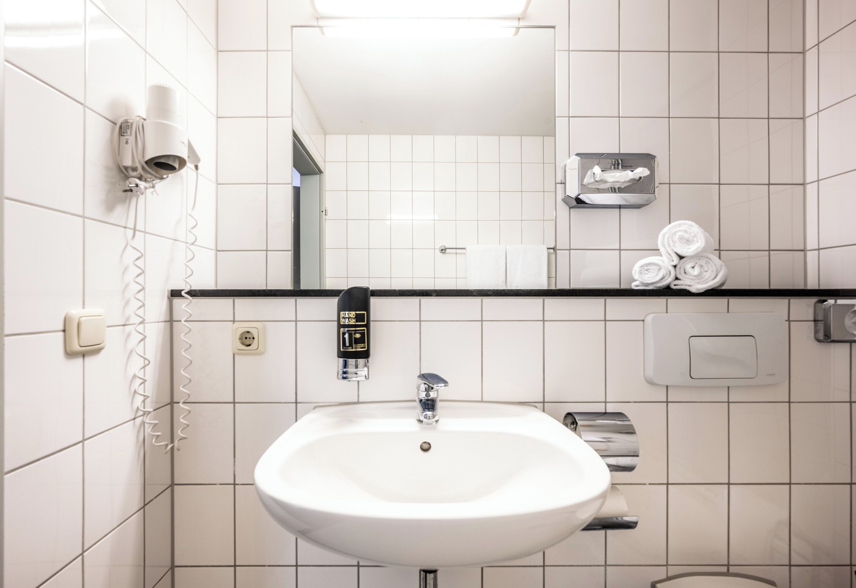 A bathroom with a white sink, a mirror, a towel rack, and a hairdryer.