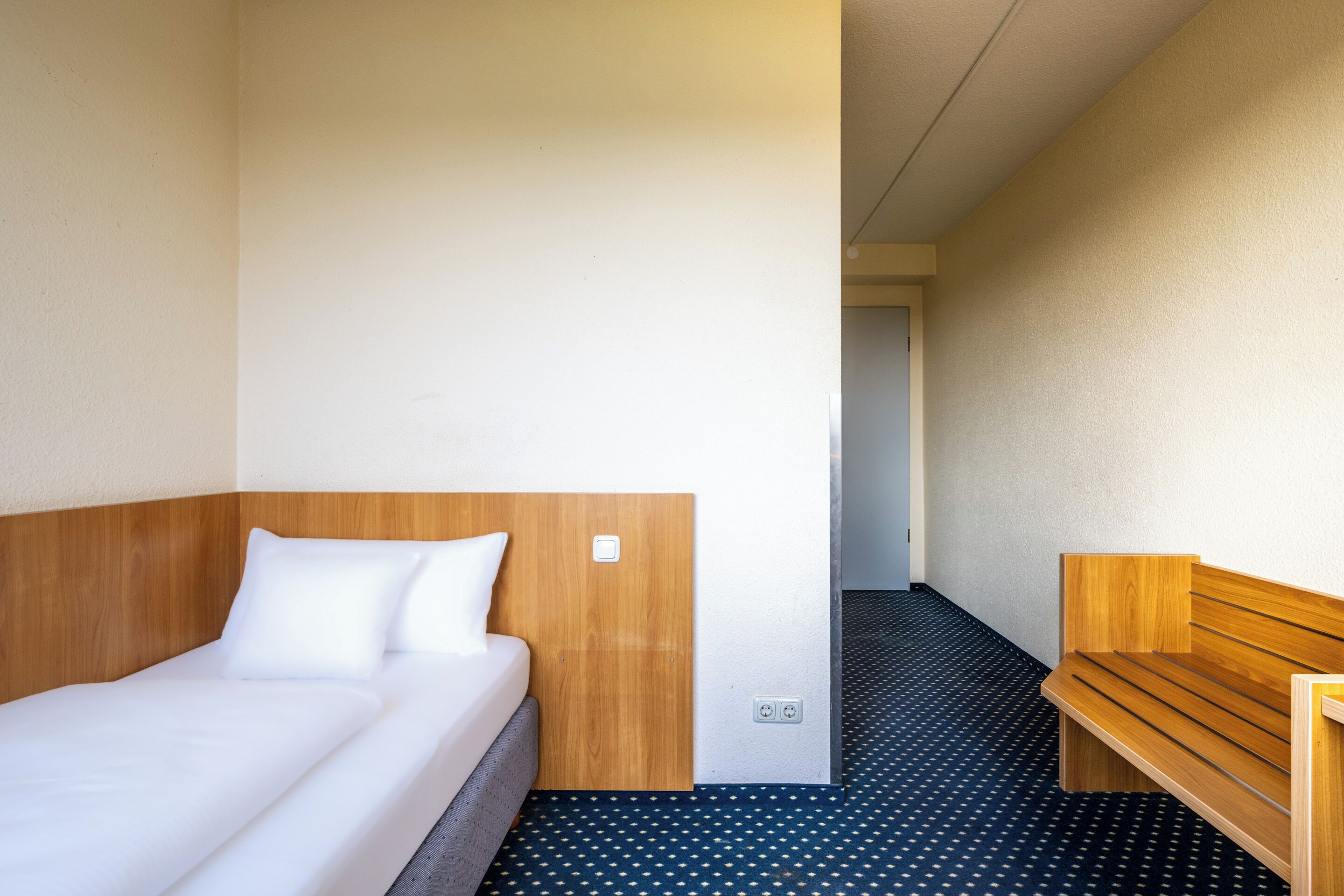 A hotel room with a wooden headboard bed, a wooden bench, and a patterned floor.