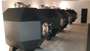 A row of industrial-style espresso machines in a modern, minimalist room with a plain wall and a door in the background. - Château Pierre de Montignac (Civrac-en-Medoc)