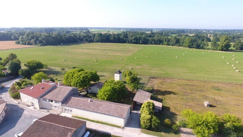 A rural property with a large open field, several buildings with red-tiled roofs, and scattered trees.