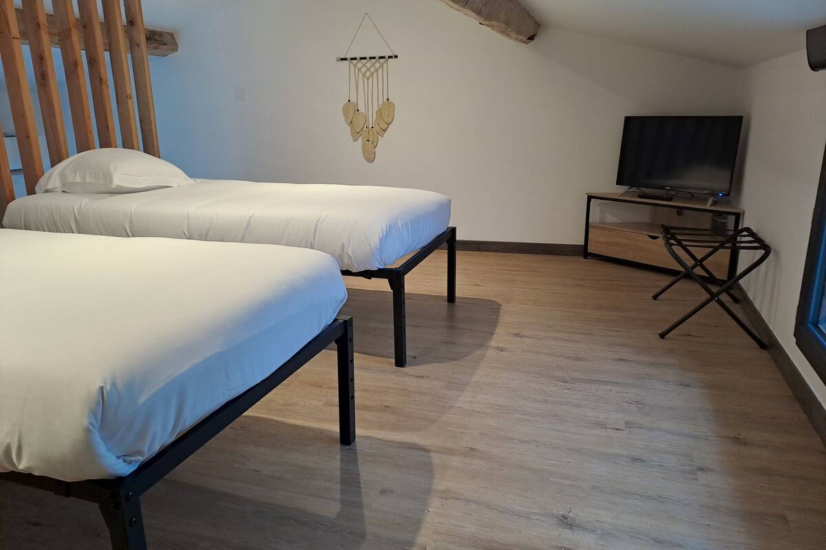Un dormitorio con dos camas, techo de madera, televisor montado en la pared y una mesita.