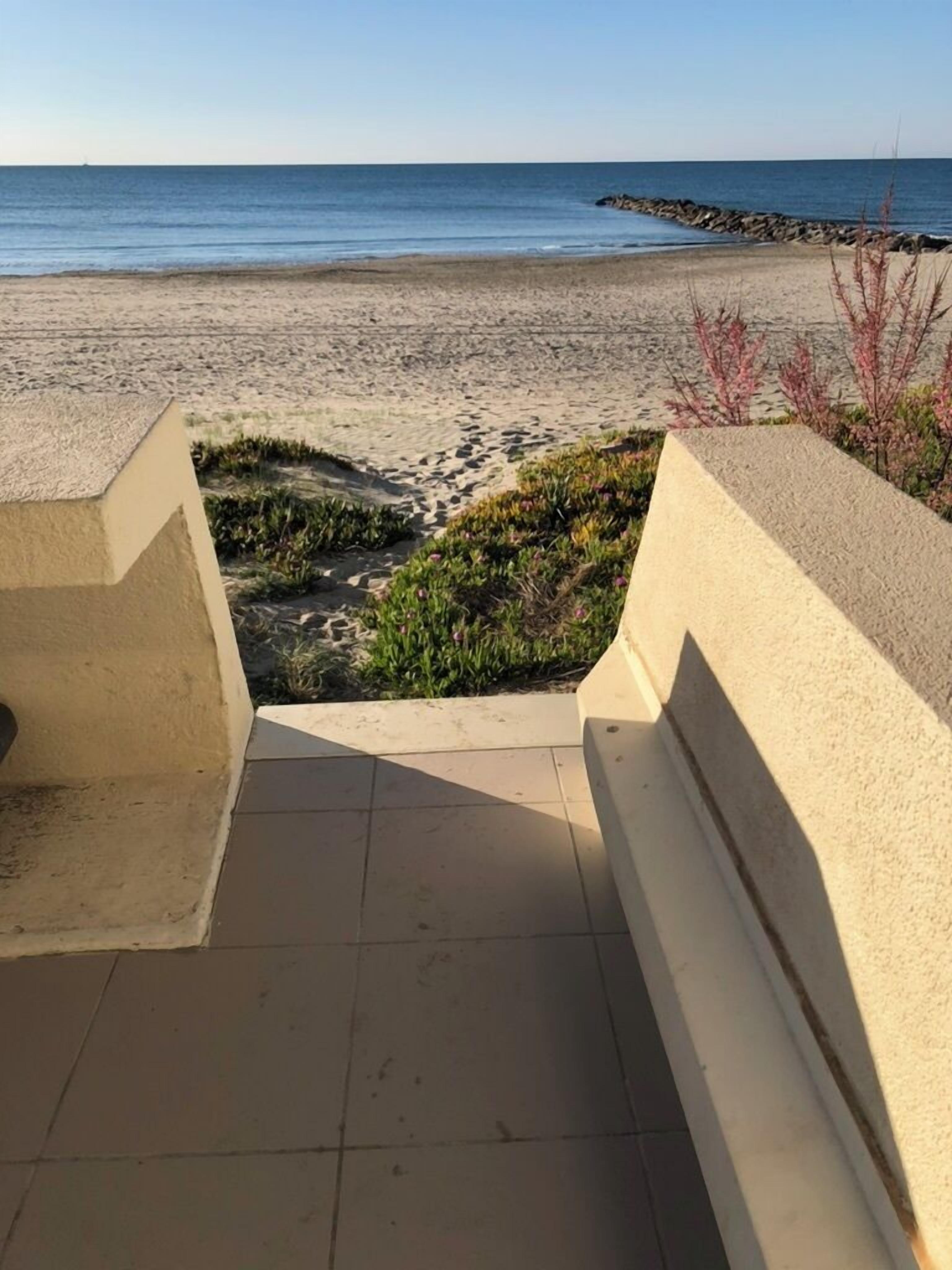 A view of a beach from a balcony with a tiled floor and a concrete railing.