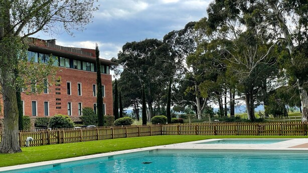 A swimming pool with a wooden fence, surrounded by well-maintained grass and trees.