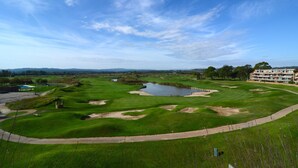 A golf course with bunkers, a pond, and a building with multiple floors.