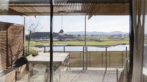 A balcony with a view of a golf course, a table, and chairs.