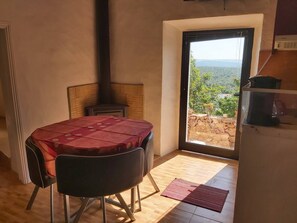 A room with a table, chairs, a fireplace, a view through a door, and a small kitchen area. - Bela Vista House - Quinta Amoreira (Loulé)