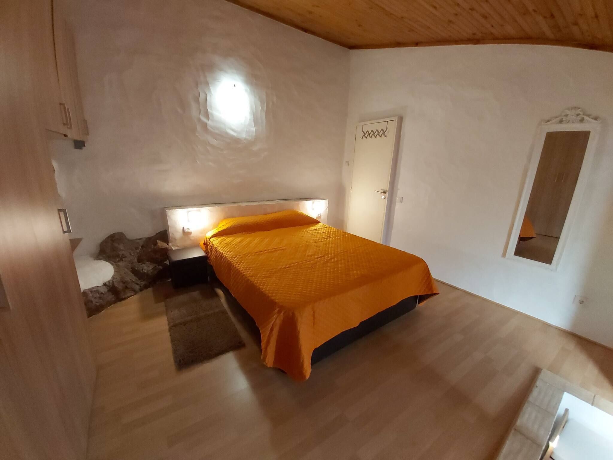 A bedroom with a bed, a nightstand, a small table, a door, and a window.