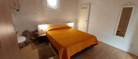 A bedroom with a bed, a nightstand, a small table, a door, and a window.