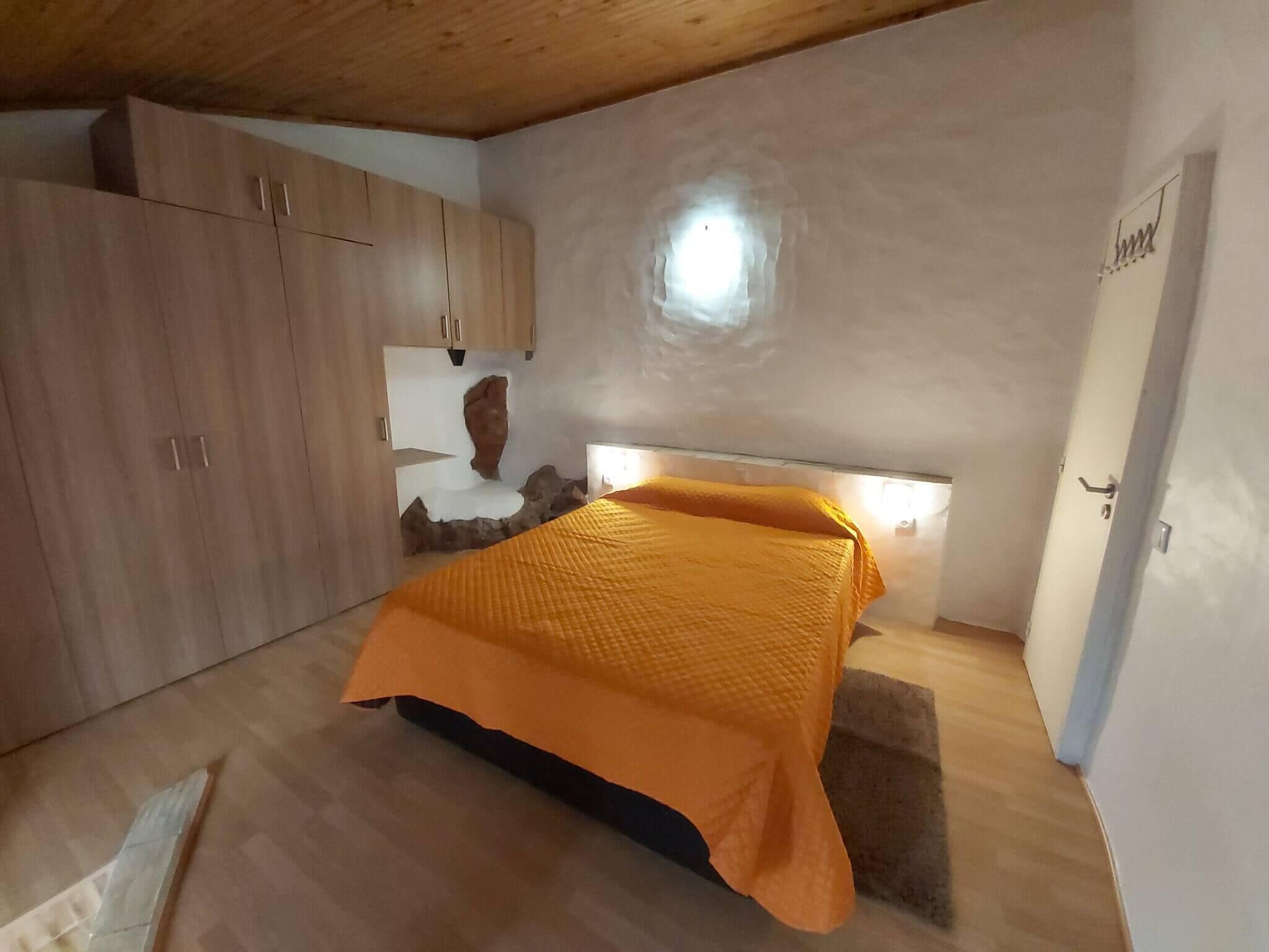 A bedroom with a bed, wooden cabinets, a stone wall feature, and a door.