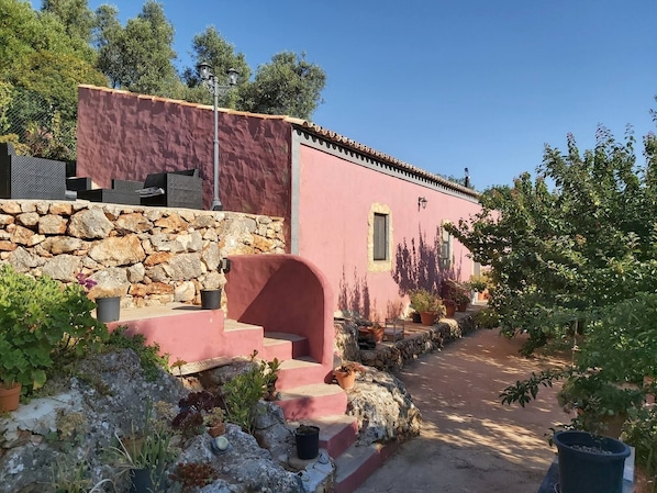 Un bâtiment rose aux murs de pierre, avec des marches menant à une porte et des plantes en pot.