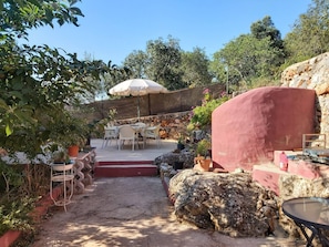 A patio area with outdoor seating, a stone wall, and a large umbrella. - Bela Vista House - Quinta Amoreira (Loulé)