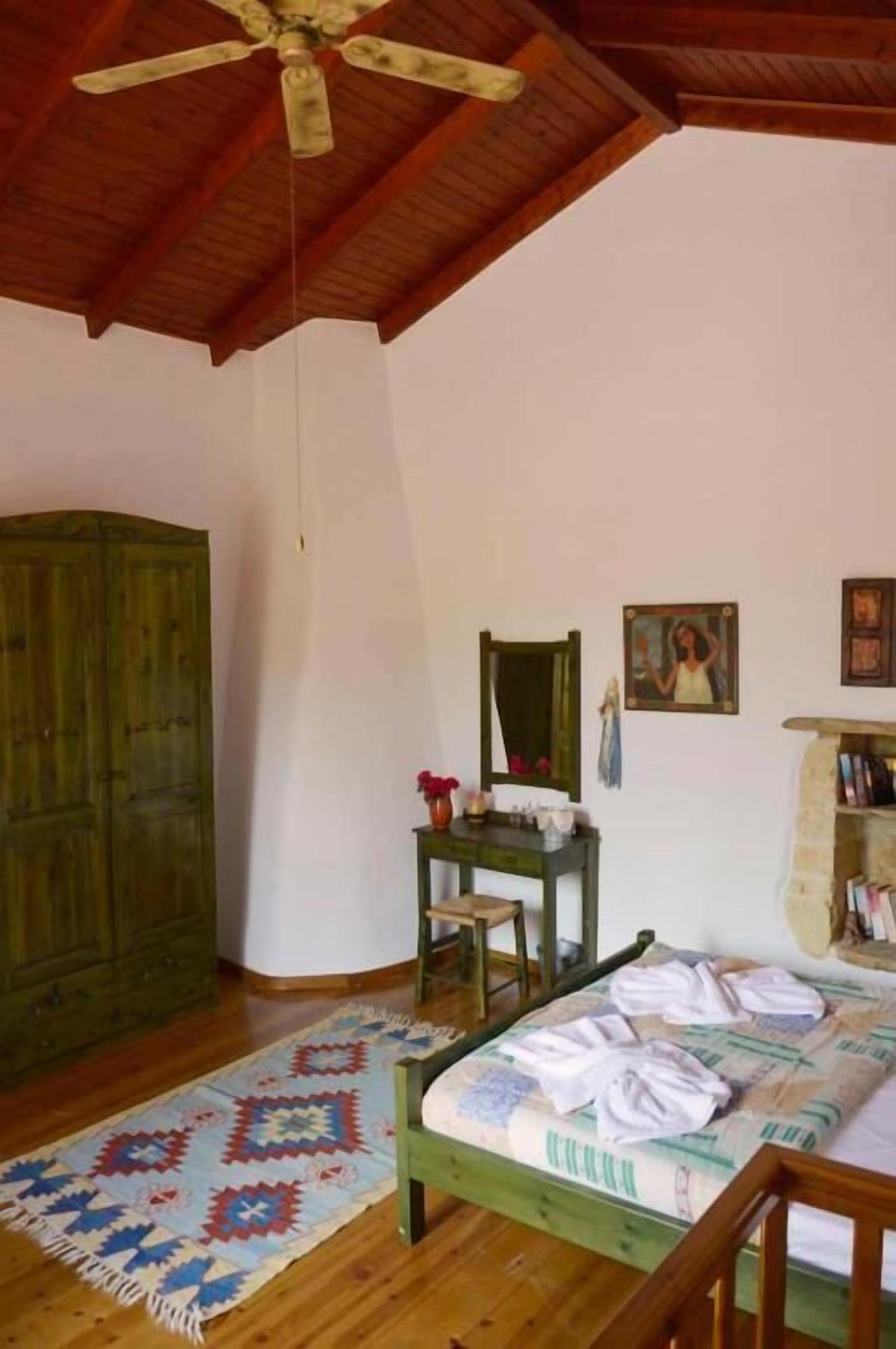 Una camera da letto con soffitto in legno, un letto con copripiumino decorato, un armadio in legno, un tavolino con specchio e una parete con quadri.