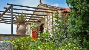 A rustic stone building with a tiled roof, a wooden fence, and a potted plant. - Apanemia Stone House in Crete (Apokoronas)