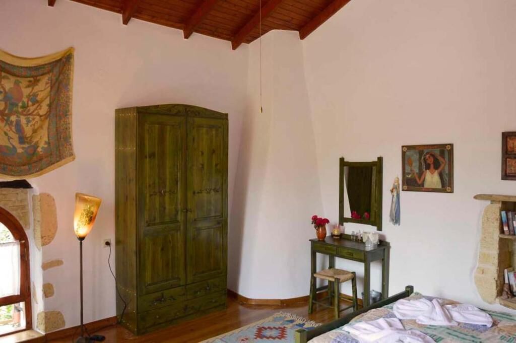 A room with a wooden wardrobe, a desk with a mirror, a bed, and a wall with religious paintings.
