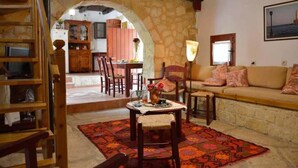 A cozy living room with a stone archway, wooden furniture, and a sofa with cushions. - Apanemia Stone House in Crete (Apokoronas)