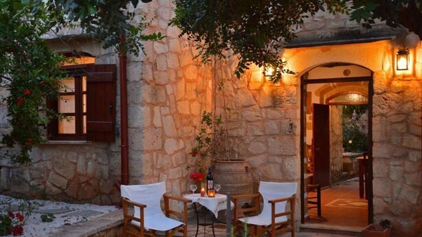 A stone building with a rustic outdoor seating area, a wooden table, and a barrel. - Apanemia Stone House in Crete (Apokoronas)