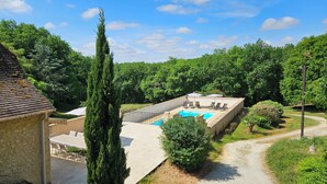 Un área de piscina con vista al bosque circundante, un edificio de piedra y un sendero.