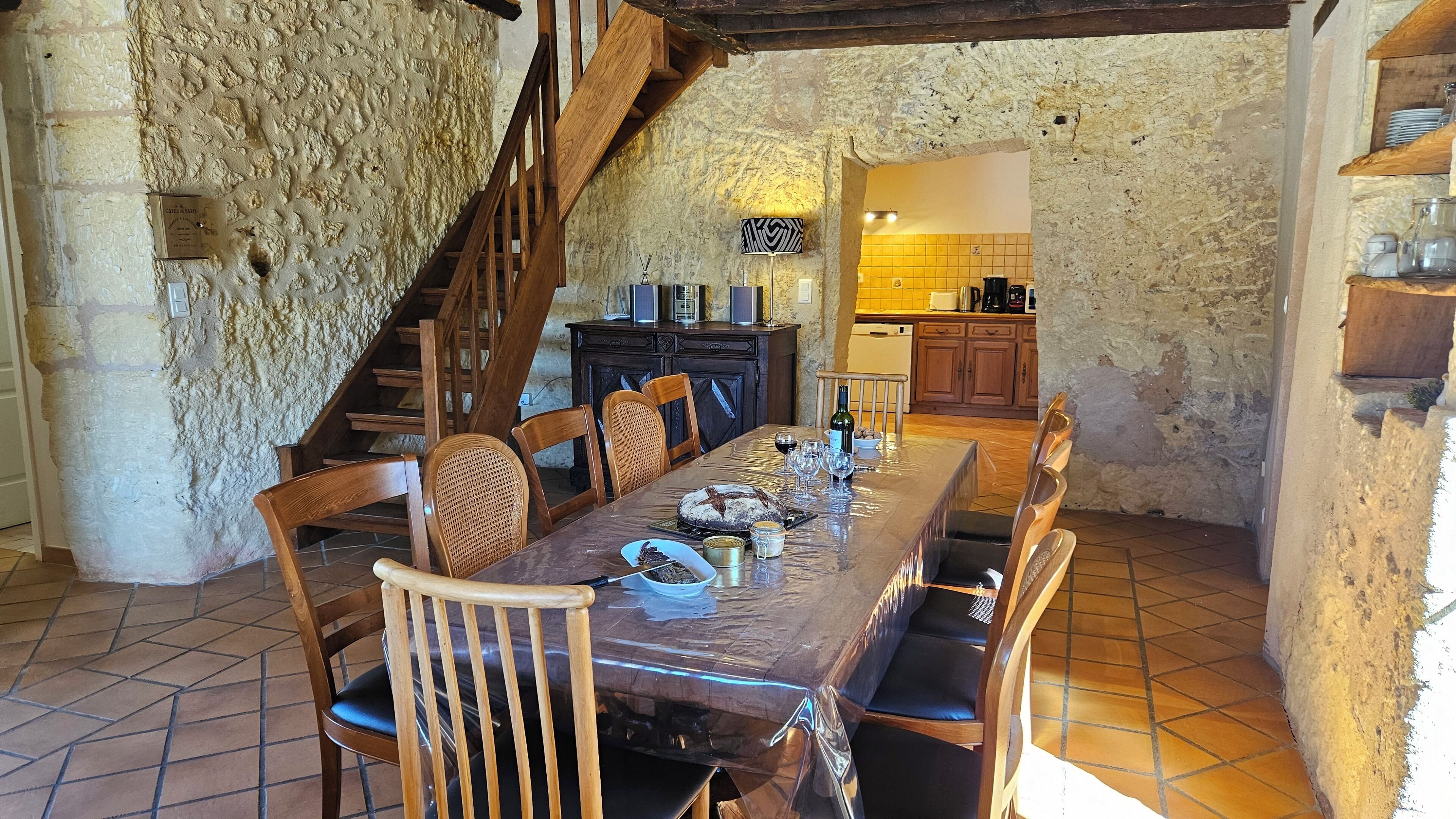 A rustic dining area with a long wooden table, chairs, and a staircase leading to an upper level.