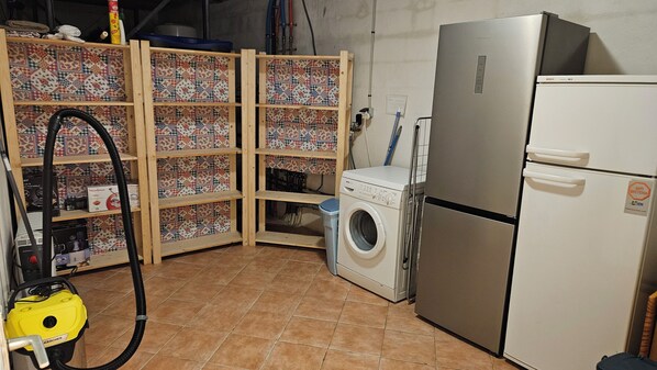Een compacte keuken met een wasmachine, een koelkast en een houten kastje met een mozaïek van tegels.