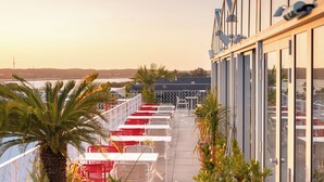 A terrace with tables and chairs, potted plants, and a view of the sea. - Hôtel Vertime (Les Sables-d'Olonne)