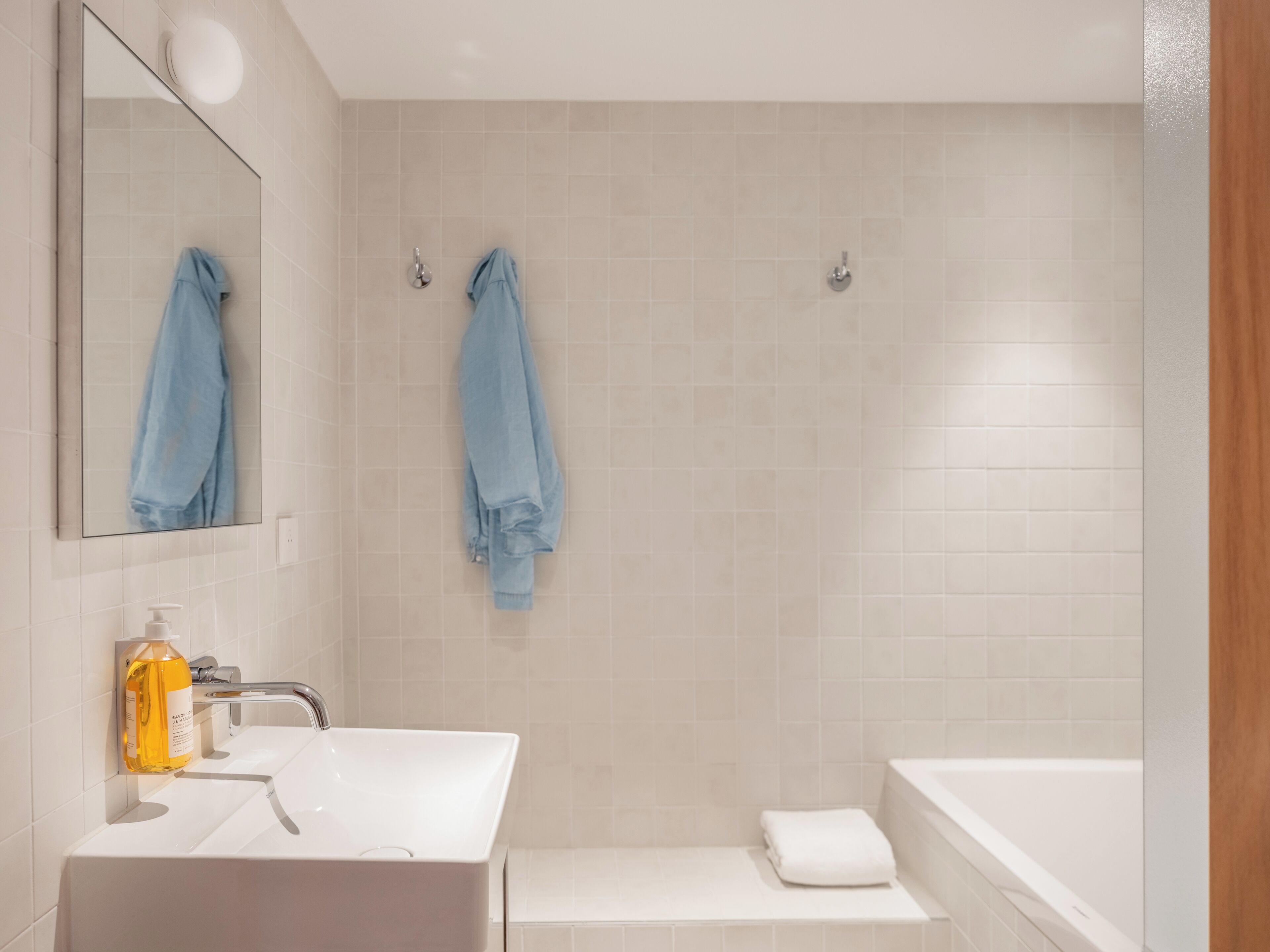 Une salle de bain avec un lavabo blanc, un miroir, un porte-serviettes avec deux serviettes, un flacon de savon et une baignoire.