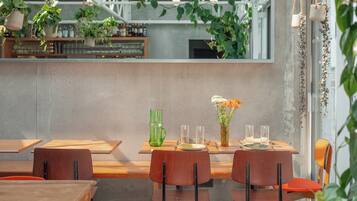 A modern dining area with wooden tables and chairs, a green vase with flowers, and hanging plants.