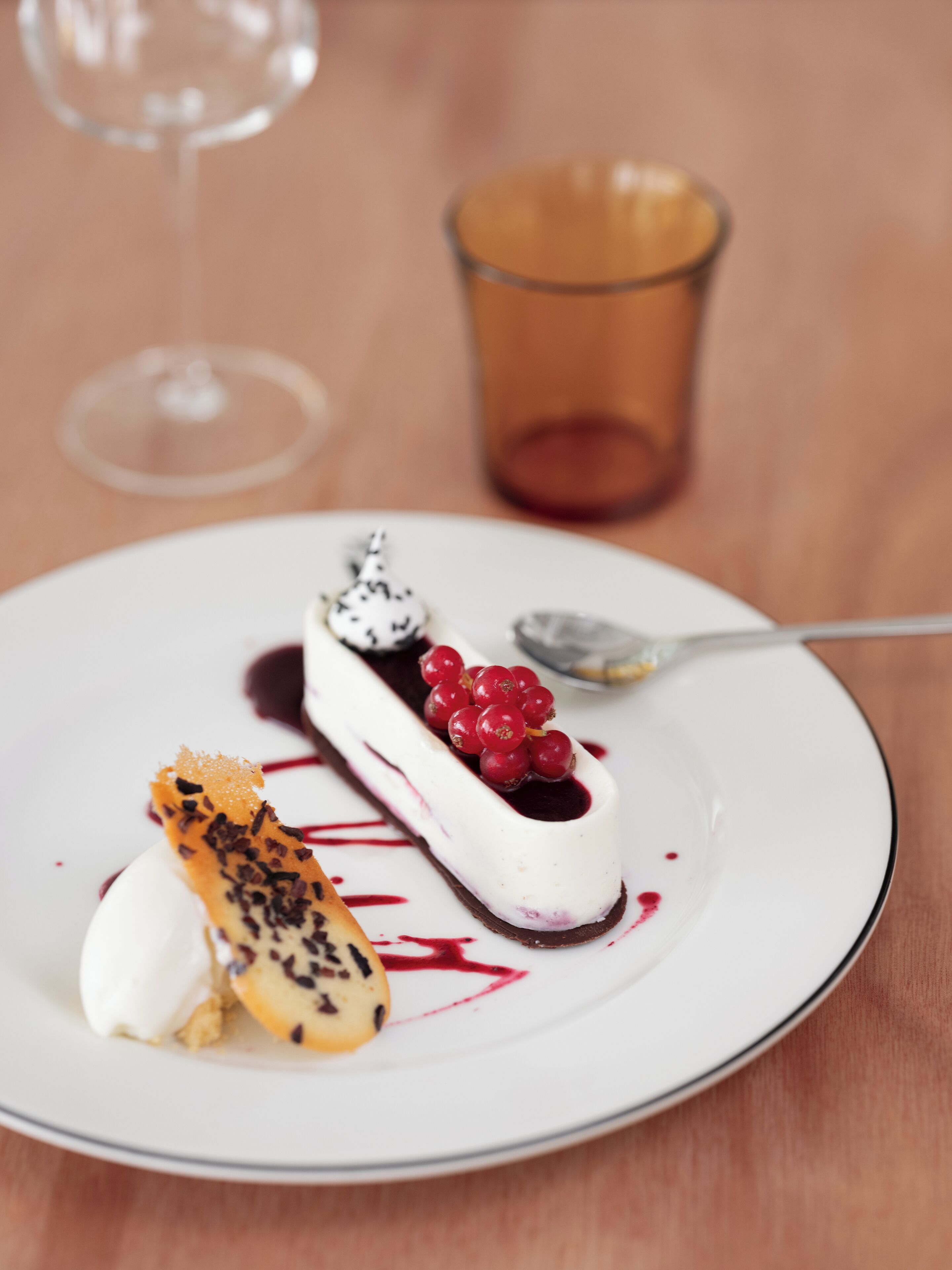 A dessert plate with a white plate, a spoon, and a glass of red liquid.