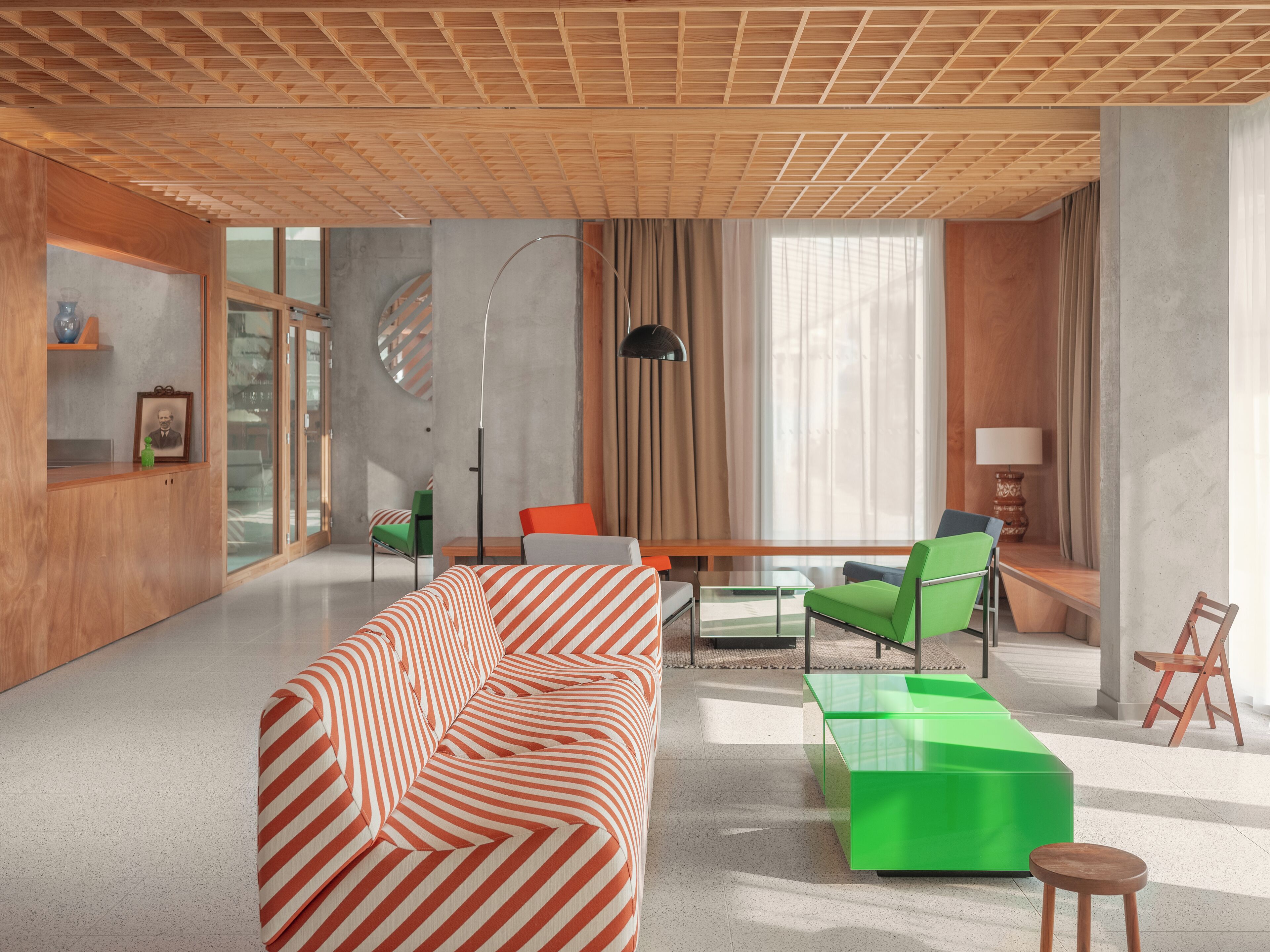 Una sala de estar moderna con un sofá a rayas, sillas verdes y una mesa de centro de vidrio.
