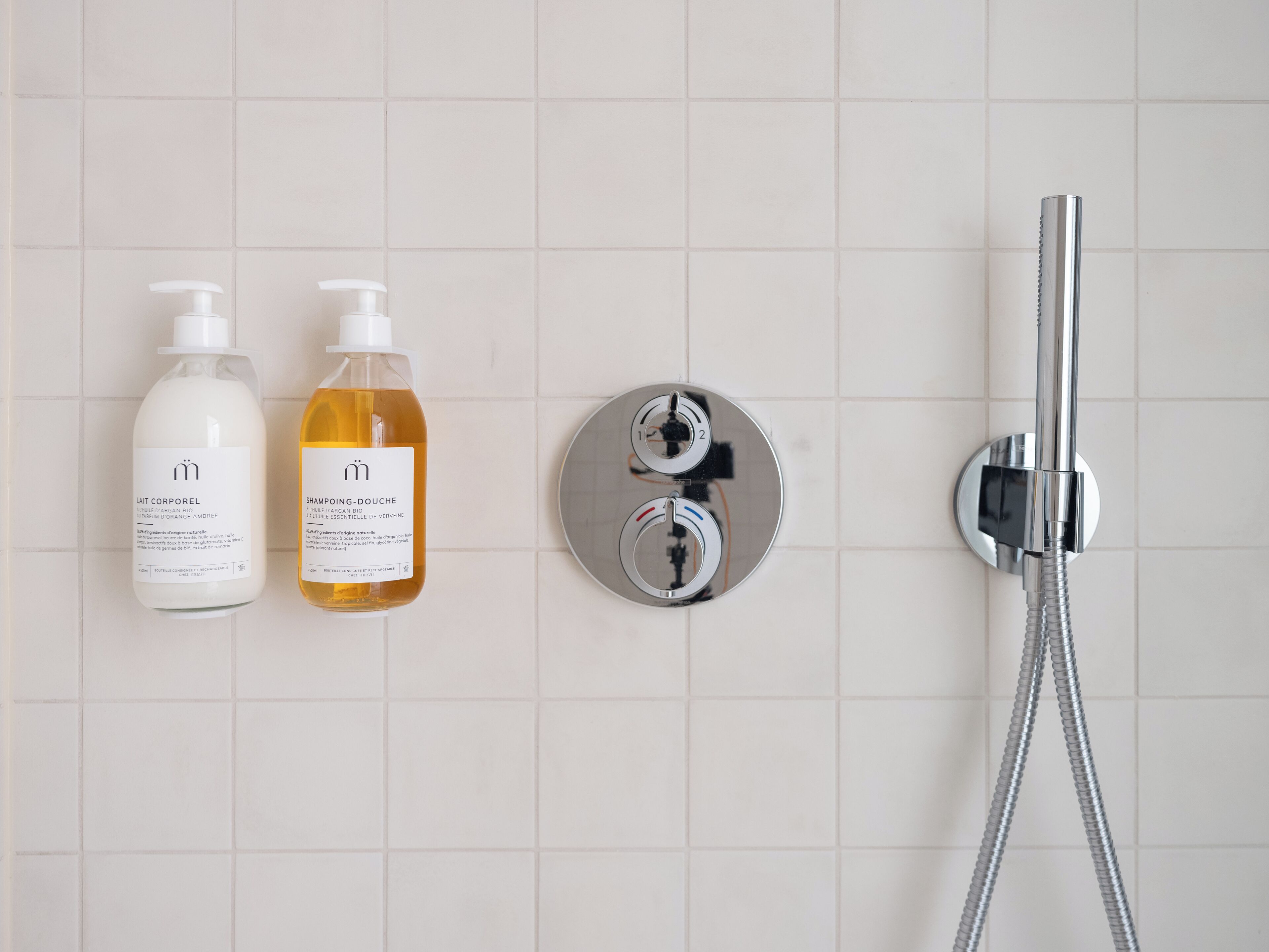 A bathroom with two bottles of shampoo and conditioner, a showerhead, and a control panel.