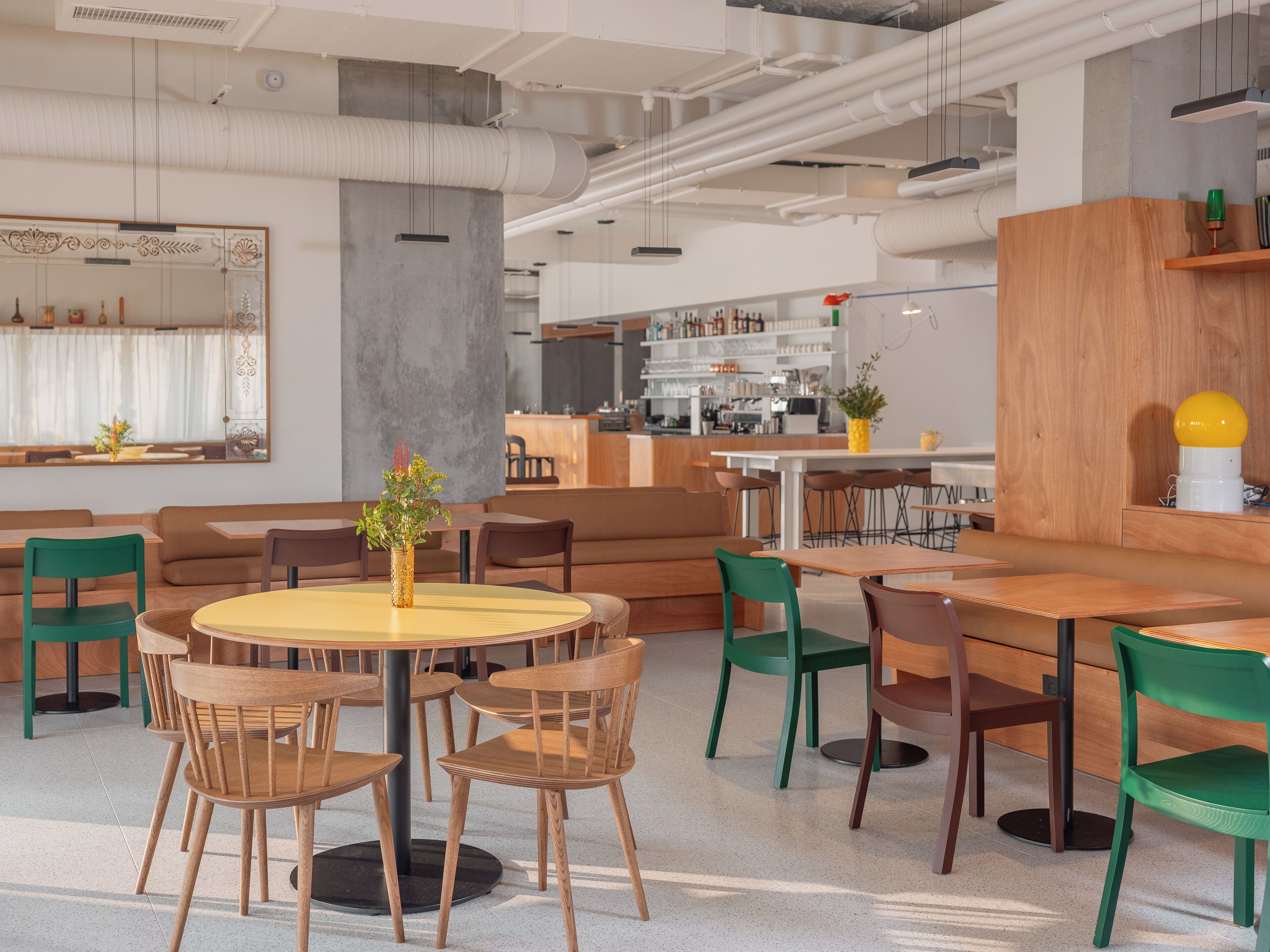 Un espace repas moderne avec des tables et des chaises rondes, une plante au centre et une cuisine en arrière-plan.