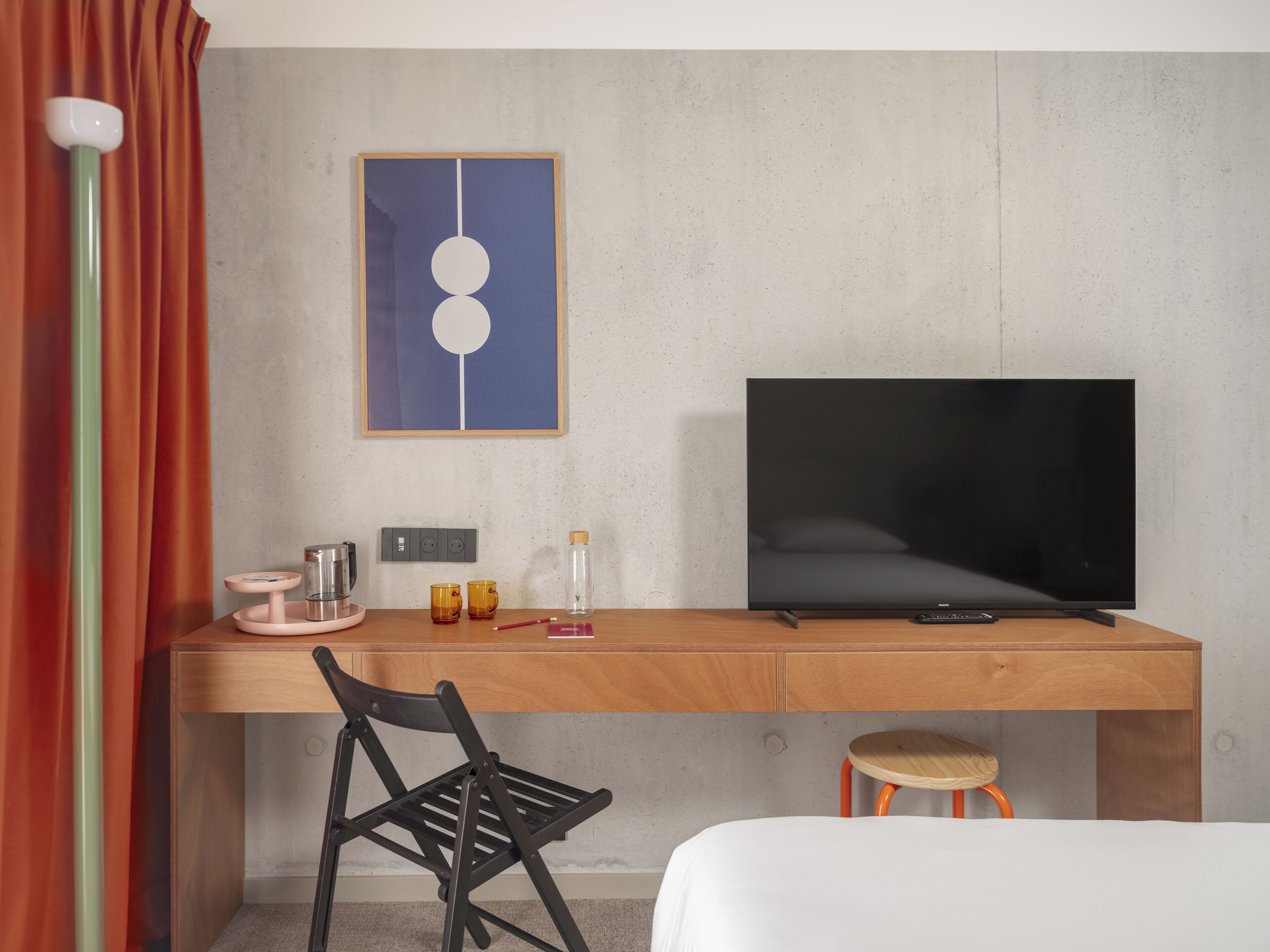 Una habitación de hotel moderna con un escritorio de madera, una silla negra, un televisor y una cama.