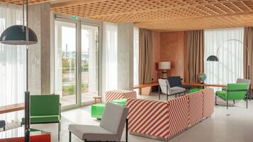 Un hall d’hôtel moderne avec un plafond en bois, de grandes fenêtres et un espace salon doté de canapés à rayures et de fauteuils verts.