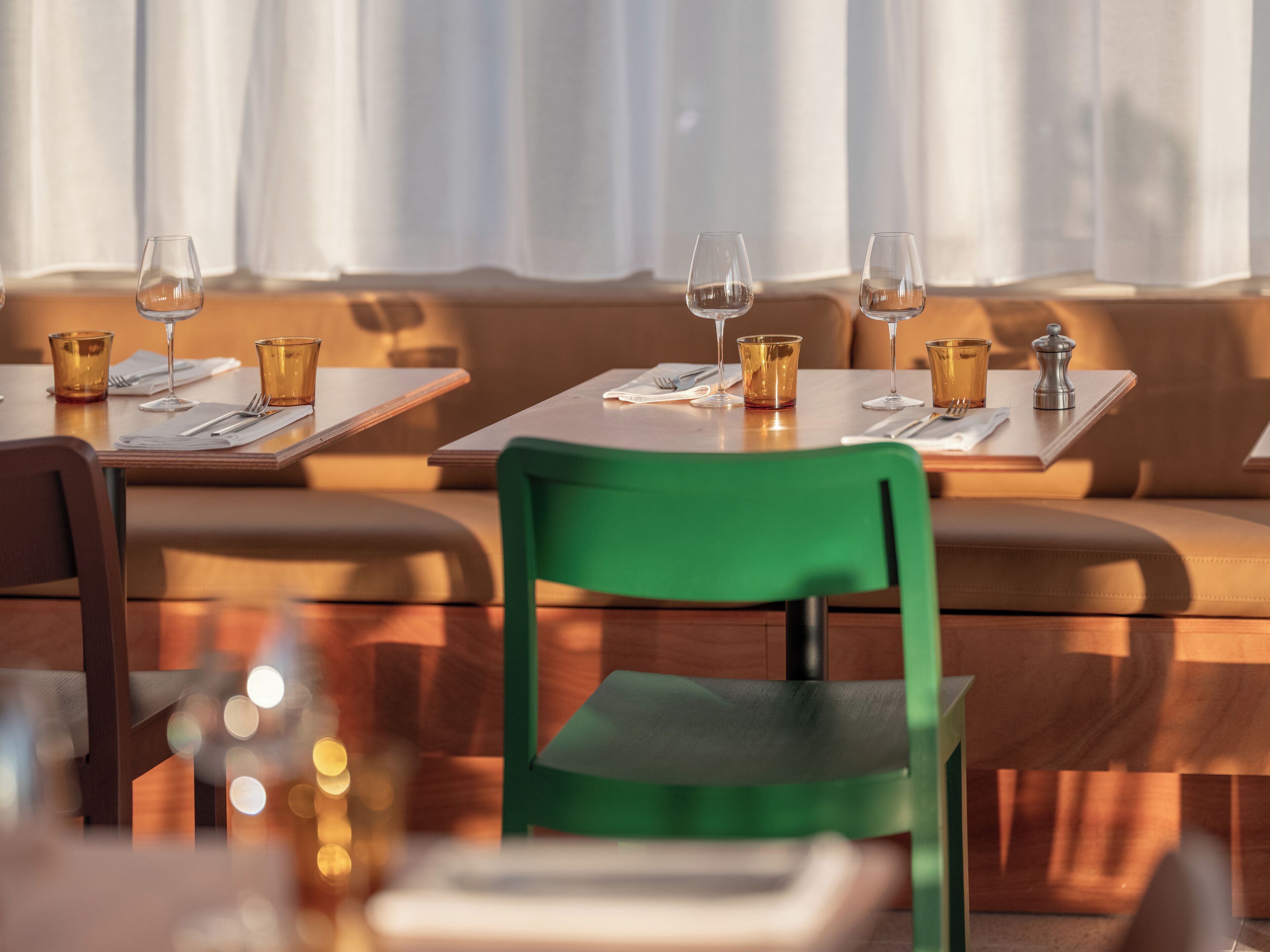 A dining area with tables set for two, each with a wine glass, a small bowl, and cutlery.