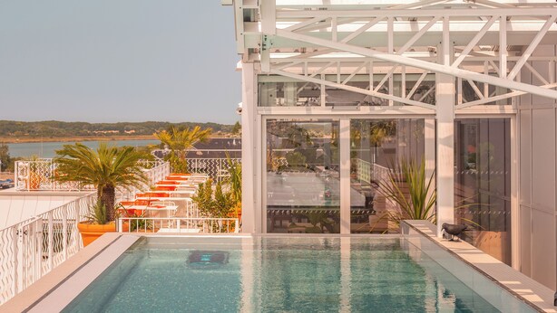 A rooftop pool with clear blue water, surrounded by white railings and orange chairs. - Hôtel Vertime (Les Sables-d'Olonne)