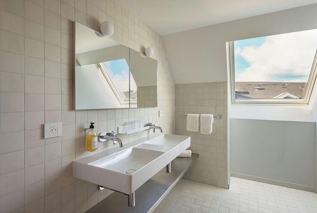 Ein modernes Badezimmer mit Dachfenster, zwei Waschbecken, einem großen Spiegel und einem Handtuchhalter.