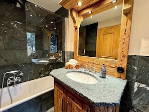 A bathroom with a large mirror, two sinks, a bathtub, and wooden cabinetry.