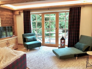 A room with a sofa, a chair, a television, and a large window with curtains.