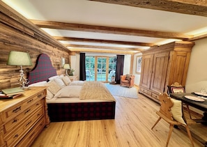 A bedroom with a bed, wooden walls, a dresser, a chair, and a table with a lamp.