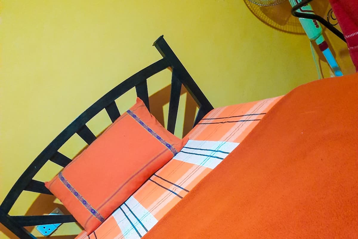 Uma cama com um cobertor laranja e uma almofada xadrez.
